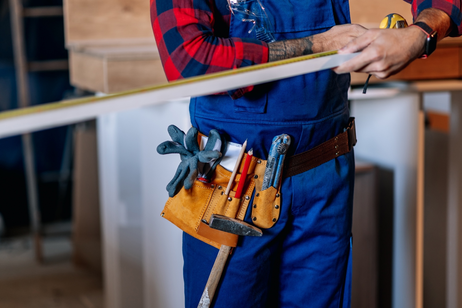 Young male carpenter working in workshop and measuring with mete